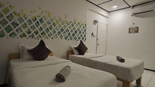 Habitación de hotel con dos camas, cada una con una almohada y una toalla enrollada.