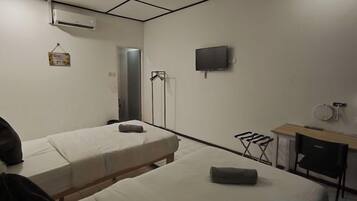 A hotel room with two single beds, a flat-screen TV, a small desk with a chair, and a window.