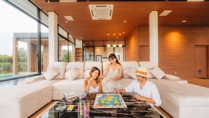 Un salon moderne doté d’un grand canapé, d’une table basse sur laquelle sont posés des jeux de société, et offrant une vue sur l’extérieur.