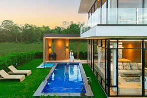 A modern house with a glass-enclosed living area, a pool, and a well-maintained lawn. - Krajokkaew Mouthten Khao Yai (Pak Chong)