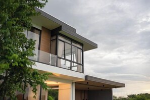 A modern two-story house with a balcony, large windows, and a flat roof. - Krajokkaew Mouthten Khao Yai (Pak Chong)