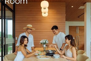 A modern dining room with a wooden ceiling, a dining table, and a group of people engaged in conversation. - Krajokkaew Mouthten Khao Yai (Pak Chong)
