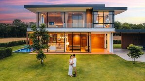 Une maison moderne à deux étages, dotée d’une grande façade vitrée, d’une piscine et d’une pelouse bien entretenue.