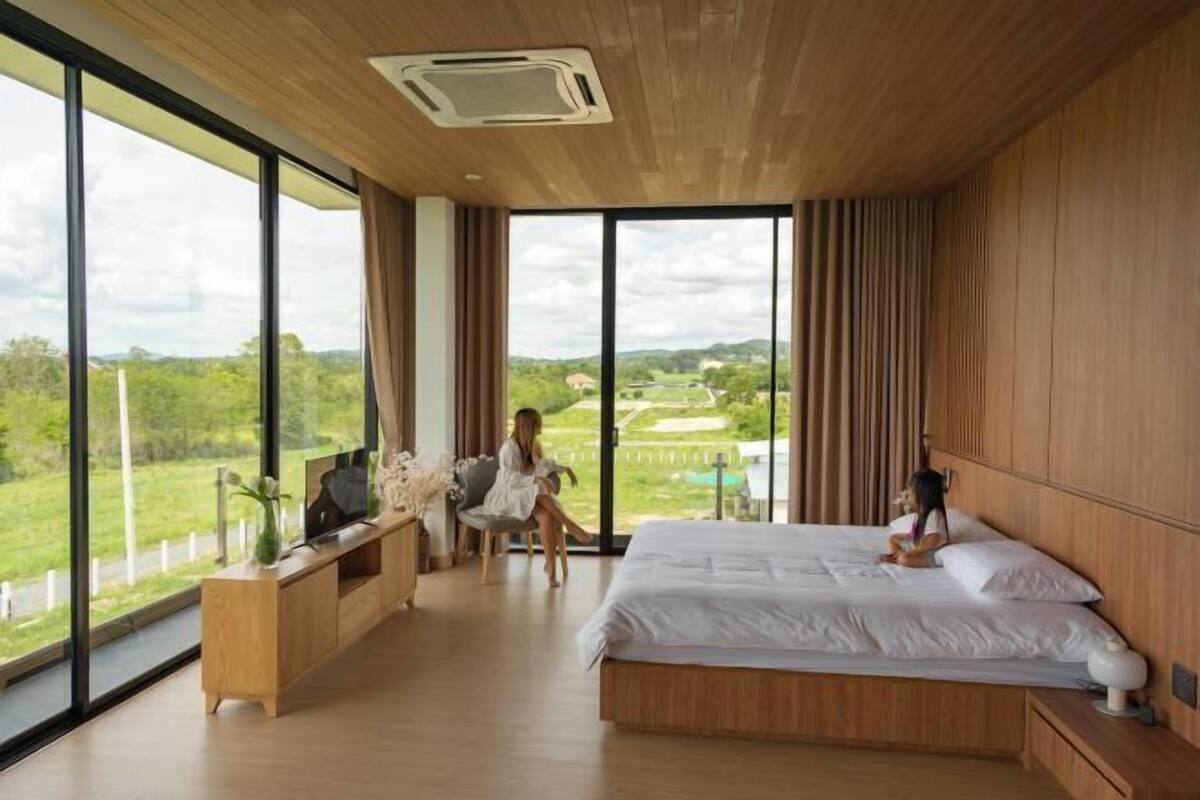 A bedroom with a large bed, a wooden desk, and a view of a green landscape.