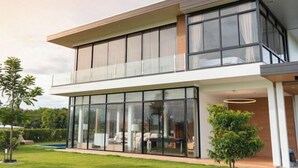Une maison moderne à deux étages, dotée de grandes fenêtres en verre, d’un toit plat et d’une pelouse bien entretenue.