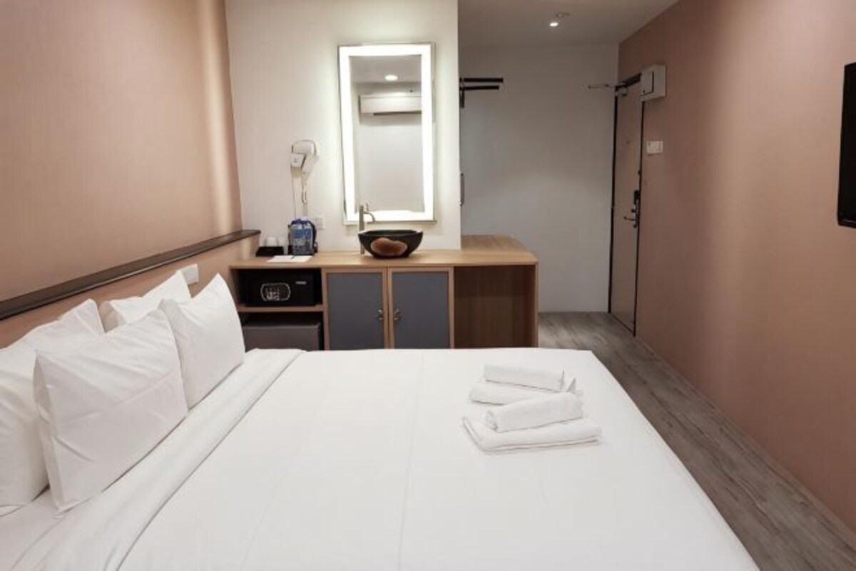 Een hotelkamer met een bed, nachtkastje met lamp, spiegel en houten dressoir.