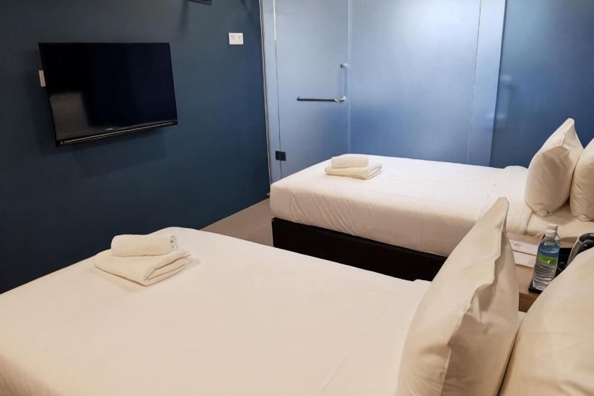 Dos camas con sábanas blancas, un televisor de pantalla plana montado en la pared y una puerta con manija.