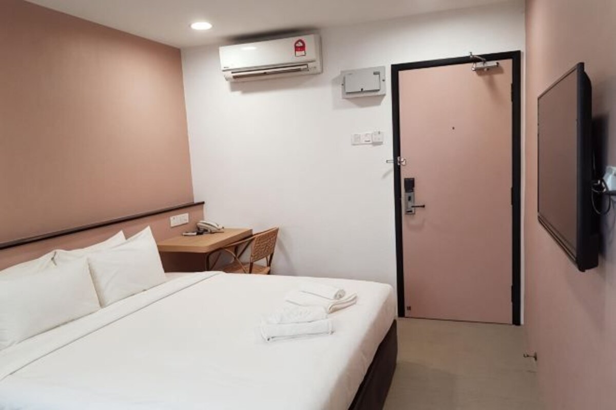 Een hotelkamer met een bed, bureau, stoel, televisie en een deur.