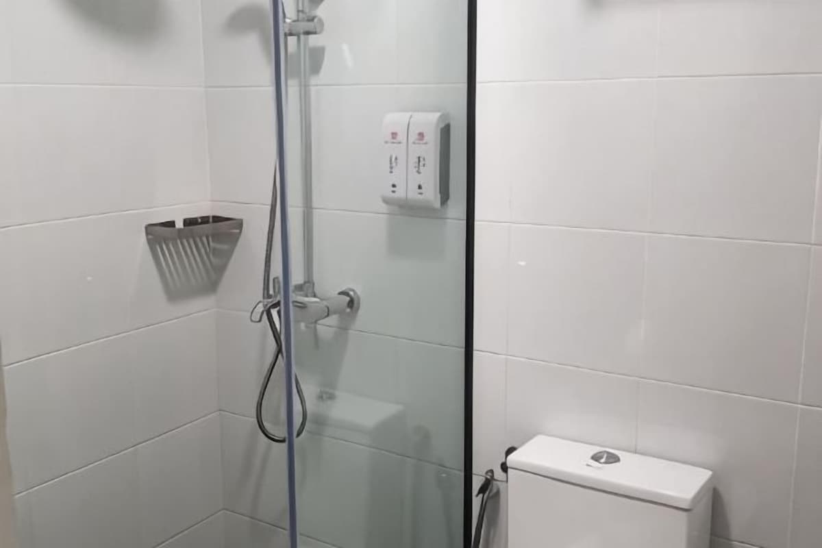 A glass-enclosed shower area with a white tiled wall, a towel rack, and a white toilet.