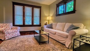 A living room with a floral armchair, a white sofa, a glass coffee table, and a lamp. - Union House - 4 bedroom century home, Uptown Waterloo (Waterloo)