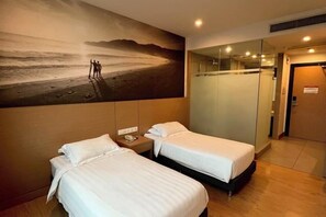 A hotel room with two beds, a painting of a beach scene, a phone on the nightstand, and a door to the right. - D Arc Hotel (Donggongon)