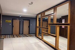 Un couloir d’hôtel avec des portes, un sol carrelé et des miroirs encadrés en bois.