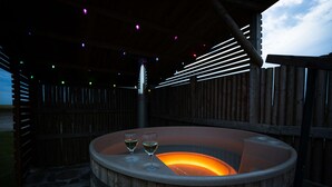 Tinaja de madera con dos copas de vino, rodeada por una terraza de madera y una estructura metálica con luces de colores.