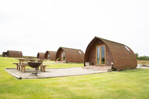 Une rangée de cabanes en bois, avec un barbecue et une table de pique-nique en premier plan.