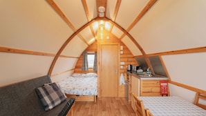 A cozy attic bedroom with a bed, a sofa, a small kitchenette, and a window.
