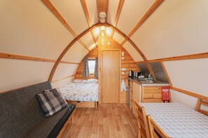 A cozy attic bedroom with a bed, a sofa, a small kitchenette, and a window. - Ensuite Cabin With A View With A Hot Tub (Camelford)