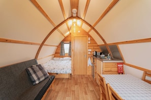 A cozy attic bedroom with a bed, a sofa, a small kitchenette, and a window.