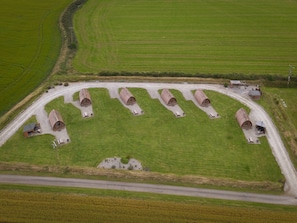 An aerial view of a rural property with six cylindrical structures, a gravel driveway, and surrounding green fields.