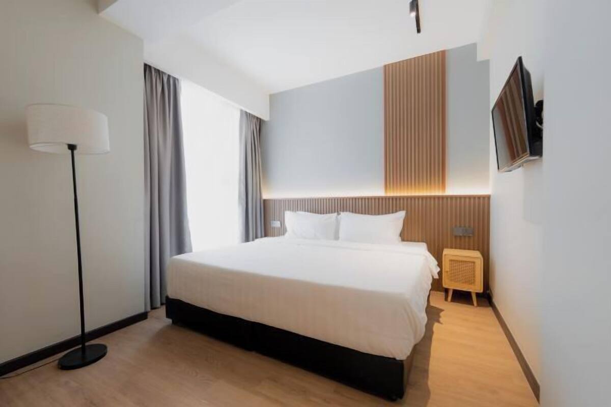 Een moderne hotelkamer met een groot bed, een staande lamp, een aan de muur bevestigde televisie en een houten hoofdbord.