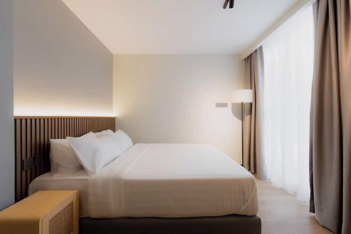Een moderne hotelkamer met een groot bed, nachtkastje, een wandlamp en een raam met gordijnen.