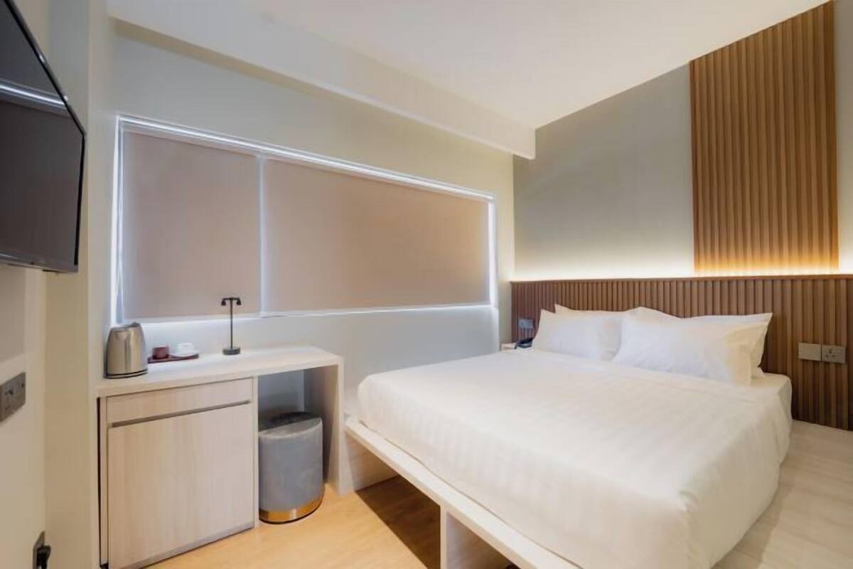 Een moderne hotelkamer met een bed, nachtkastje en een aan de muur bevestigde televisie.