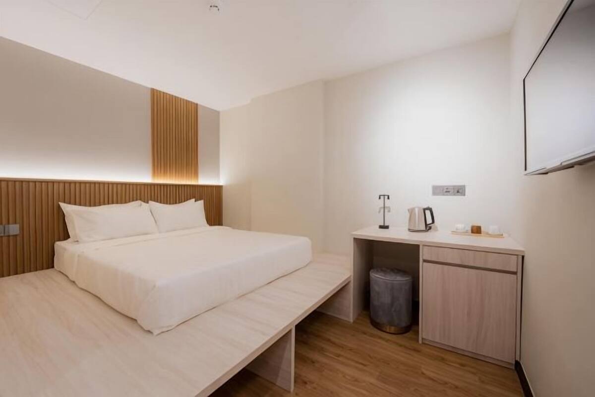 Een hotelkamer met een bed, nachtkastje en een klein bureau met een prullenbak.