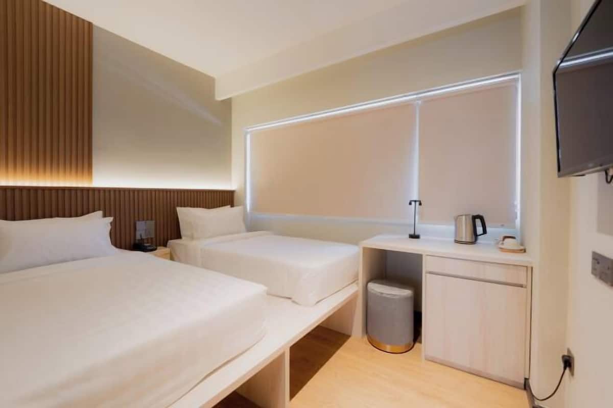 Een hotelkamer met twee bedden, een nachtkastje met een lamp, een televisie en een kleine kitchenette.