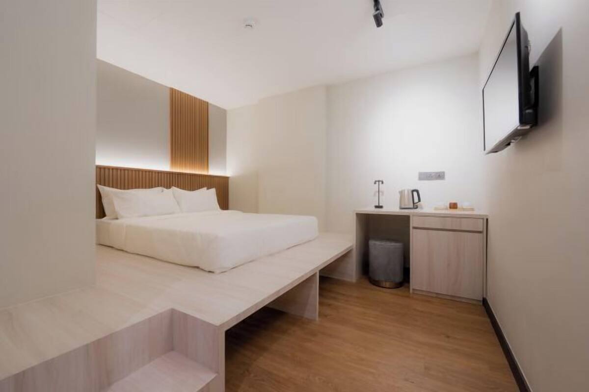 Een moderne hotelkamer met een bed, een klein bureau, een televisie en een prullenbak.
