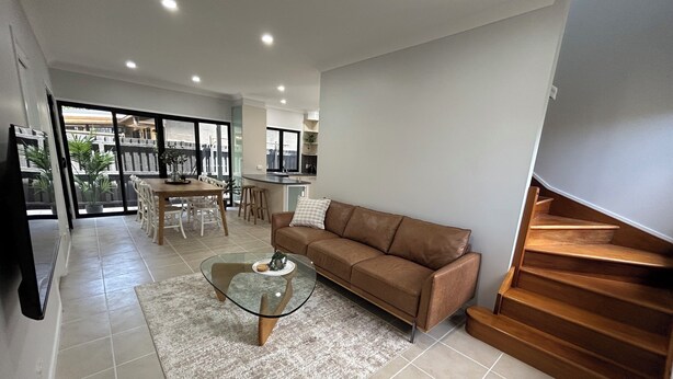 Uma sala de estar moderna com um sofá de couro marrom, uma mesa de centro de vidro e uma área de jantar com uma mesa e cadeiras de madeira.