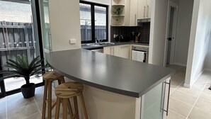 Uma cozinha moderna com uma ilha grande, banquetas de madeira e um vaso com planta.