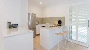 Una cocina moderna con un refrigerador de acero inoxidable, encimeras blancas y una pequeña isla con taburetes de bar.