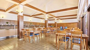 A spacious dining area with wooden tables and chairs, a kitchen in the background, and a high ceiling with exposed beams. - Bungalow in der Ferienanlage Kanegra (Buje)