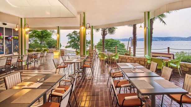 An outdoor restaurant with tables and chairs, overlooking a body of water. - Bungalow in der Ferienanlage Kanegra (Buje)