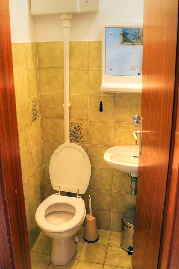 A small bathroom with a toilet, sink, and a trash can. - Ferienwohnung mit Terrasse (Crikvenica)