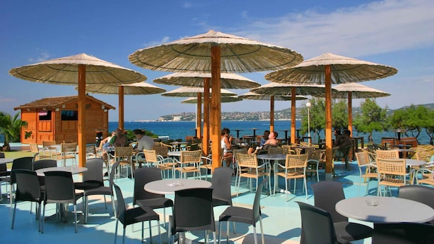 An outdoor seating area with tables and chairs, surrounded by thatched umbrellas, overlooking a body of water. - Bungalow in der Ferienanlage Kanegra (Buje)