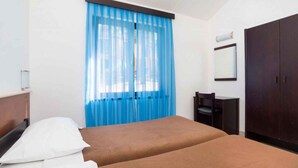 A hotel room with two beds, a desk, a chair, a wardrobe, and a window with blue curtains. - Bungalow in der Ferienanlage Kanegra (Buje)