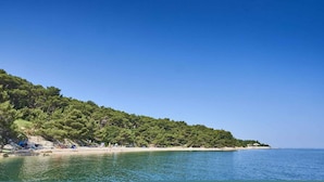 A beach with clear blue water, a sandy shore, and a forested hill. - Bungalow in der Ferienanlage Kanegra (Buje)
