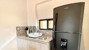 Une cuisine compacte avec un réfrigérateur noir, des placards en bois, un plan de travail avec un évier et une fenêtre située au-dessus de l’évier.