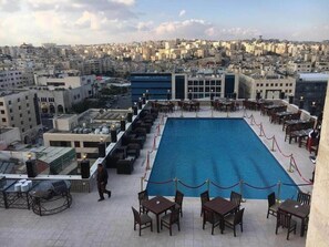 A rooftop pool area with tables and chairs, surrounded by a cityscape view. - Arena Space Hotel (Amman)