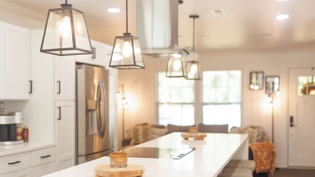 Una cocina moderna con una isla central, iluminación colgante y un refrigerador de acero inoxidable.