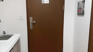 A hotel room with a wooden door, a small window, a black mat at the entrance, and a white countertop with a sink.