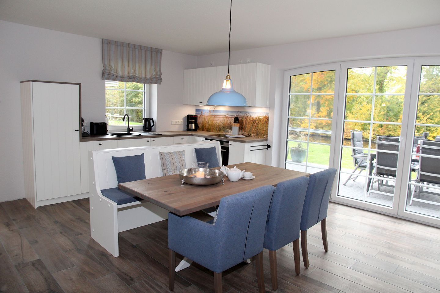 Een moderne keuken met een eetgedeelte, een blauwe hanglamp en uitzicht op de omgeving.