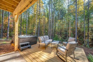 Une terrasse en bois avec un jacuzzi, un canapé et deux fauteuils à bascule, le tout entouré d’une forêt.