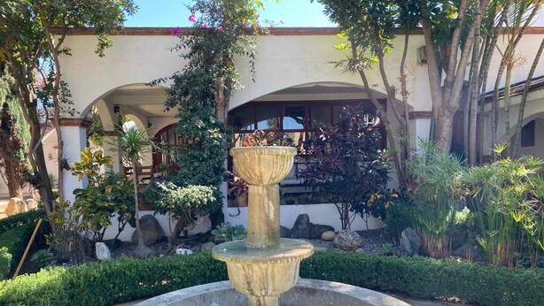 A stone fountain with water in a circular basin, surrounded by greenery and a building with arches in the background. - Bule Villas, 1Bed/1Bath;
El Cielito Lindo: fitness room, heated pool, WiFi  (San Francisco Tutla)
