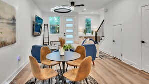 Ein modernes Wohnzimmer mit Essbereich, ausgestattet mit Deckenventilator, Einbaustrahlern und einem großen Wandbild.