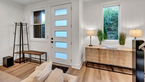 Ein modernes Wohnzimmer mit Holzboden, einer Couch, einem Couchtisch, einer Kommode mit Pflanzen und einer Tür mit Sandstrahlglas.