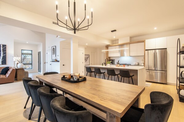 Una cocina moderna con una mesa de comedor de madera, sillas negras y electrodomésticos de acero inoxidable.