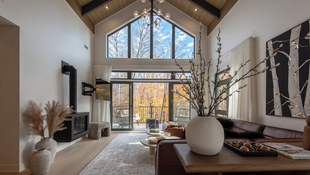 A spacious living room with a high ceiling, large windows, a fireplace, and a cozy seating area.