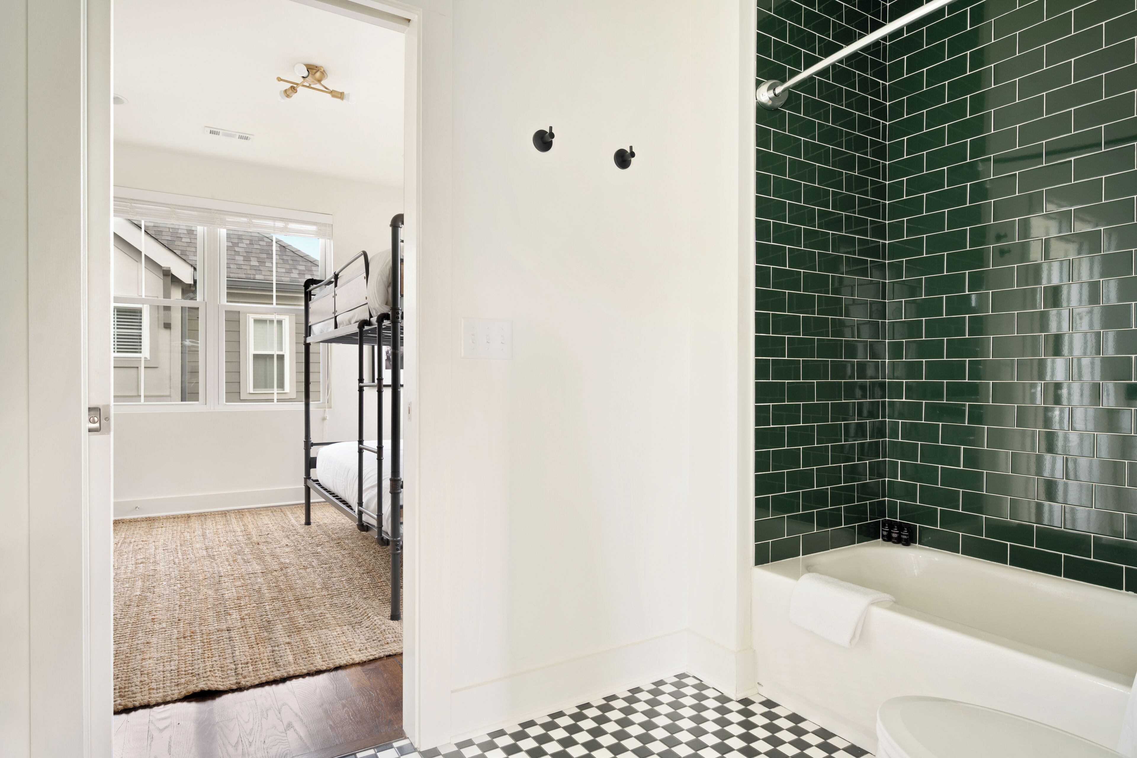 A bathroom with a checkered floor, a bathtub, and a green-tiled shower area.