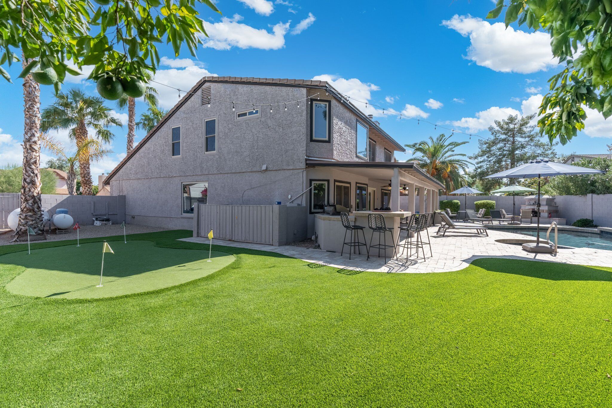 Una casa con un patio trasero que incluye piscina, mobiliario exterior y un campo de práctica de golf.